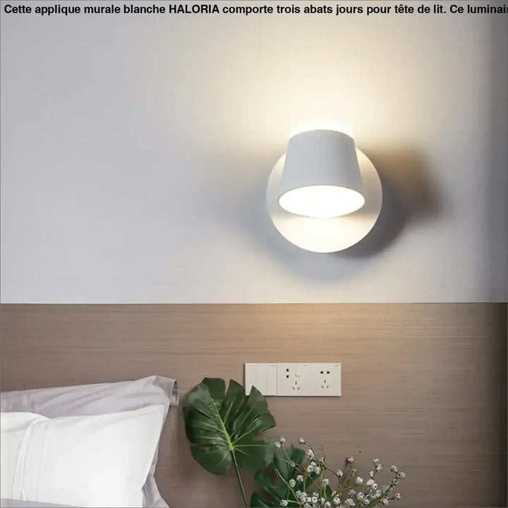 Applique murale blanche avec trois abats jours cylindriques diffusant une lumière douce pour tête de lit haloria