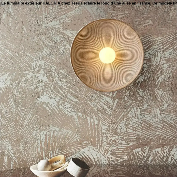 Luminaire exterieur haloria avec applique murale circulaire en rotin tressé diffusant une lumière chaude le long dune allée