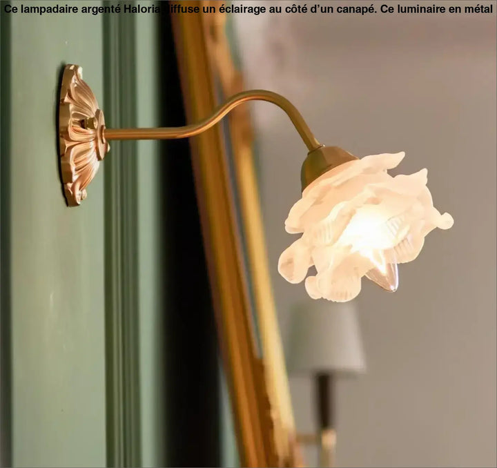 Lampadaire argente en laiton antique avec abat-jour en verre blanc translucide en forme de rose côté d’un canapé