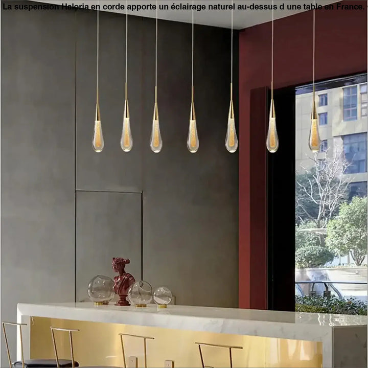 Cinq lampes suspendues corde haloria dorées avec abat-jour en verre en forme de goutte au-dessus d’une table ou d’un coin salon