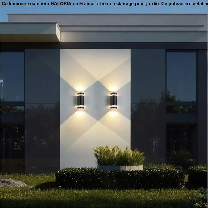 Poteau pour luminaire exterieur haloria avec appliques murales cylindriques noires et éclairage chaud côté d’un canapé