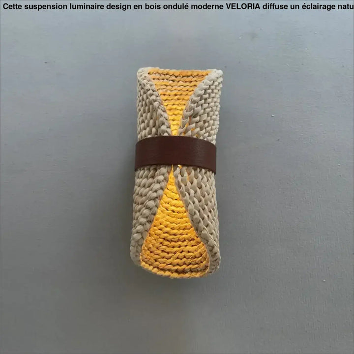 Une serviette roulée tricotée à la main en jaune vibrant et beige neutre avec une lanière en cuir brun pour luminaire design bois ondule moderne veloria