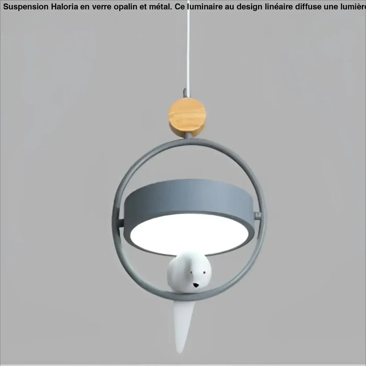 Suspension luminaire lineaire en verre opalin avec cadre métallique circulaire, abat-jour gris et oiseau céramique blanc au-dessus d’une table