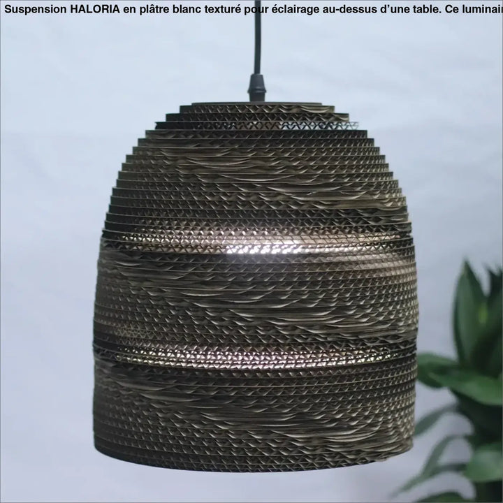 Suspension luminaire moderne en platre texture blanc au-dessus d’une table avec abat-jour en carton ondulé bronze ajouré