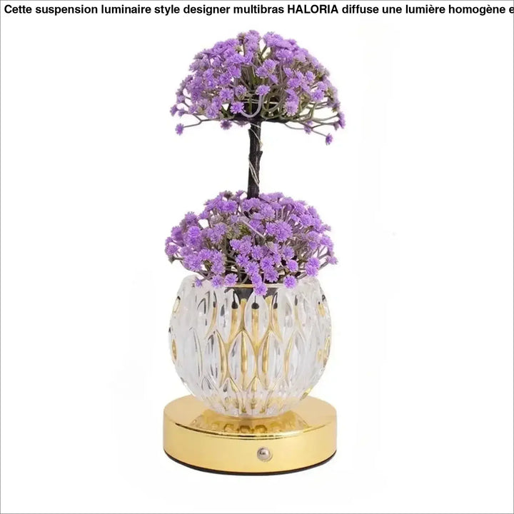 Lampe de table tulyna avec base en verre facetté clair, accents dorés, et source lumineuse ornée de fleurs violettes artificielles